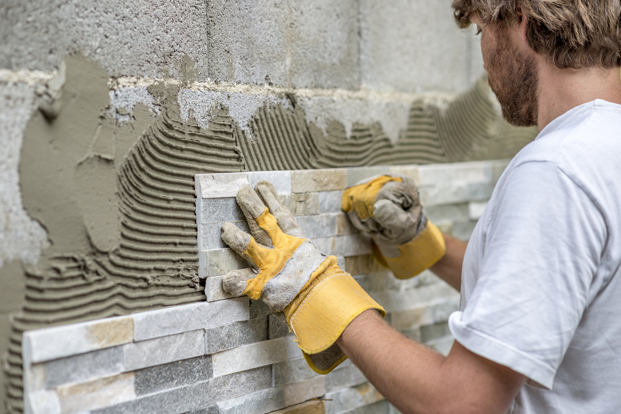 Man pressing ornamental tile into a glue on a wall